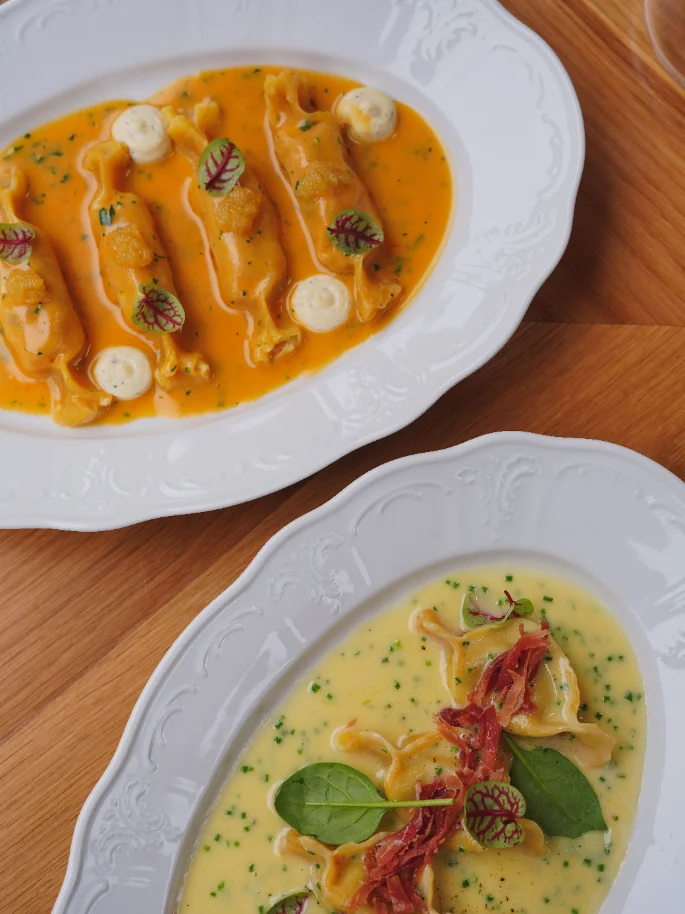 Dois pratos de massa recheada, um em molho de marisco e outro num creme com presunto